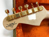 Back of Fender Custom Shop guitar headstock with gold tuning pegs on natural wood finish inside orange plush case
