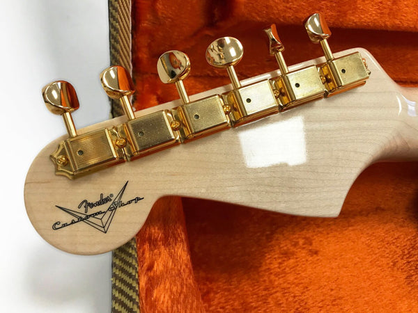 Back of Fender Custom Shop guitar headstock with gold tuning pegs on natural wood finish inside orange plush case