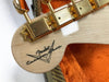 Close-up of Fender Custom Shop guitar headstock with gold tuning pegs and logo on light wood finish, inside orange plush guitar case.