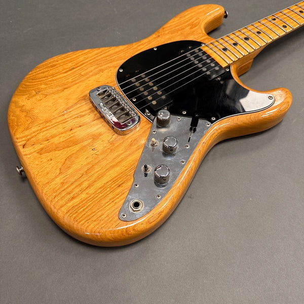 Electric guitar with natural wood finish, black pickguard, chrome knobs, and a maple neck on gray background