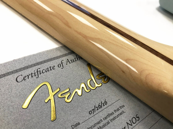 Close-up of Fender Certificate of Authenticity with violin-style guitar neck resting on top, highlighting the gold Fender logo and wood grain of the neck.