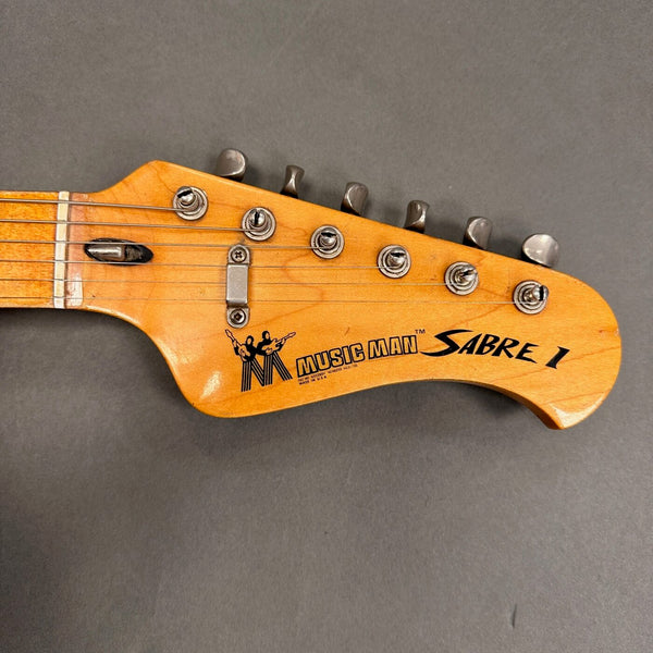 Close-up of Music Man Sabre 1 electric guitar headstock with tuning pegs and logo on natural wood finish