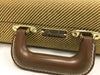 Close-up of Fender guitar case handle with brown leather grip and tweed fabric exterior featuring Fender logo plaque
