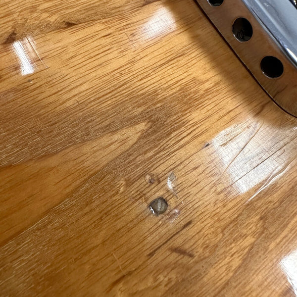 Close-up of light brown wood grain and finish on electric guitar body with metal plate and screws.