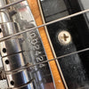 Close-up of guitar bridge and metal saddle with serial number 092424 visible on chrome plate, showing wound strings and black pickguard with screw.