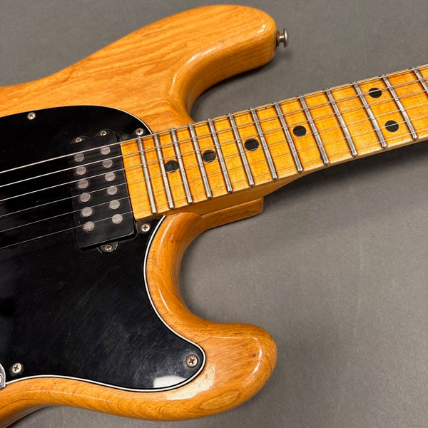 Close-up of natural finish electric guitar body and maple neck with black pickguard and humbucker pickup on gray background
