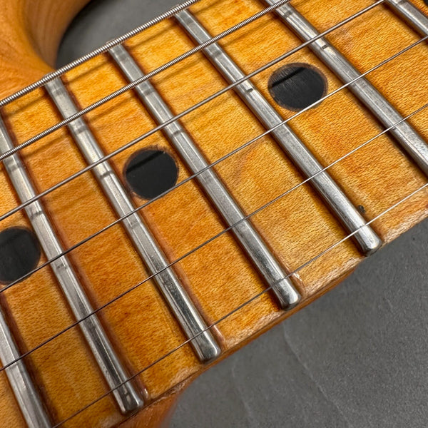 Close-up of maple guitar fretboard with metal frets, black dot inlays, and steel guitar strings on dark background