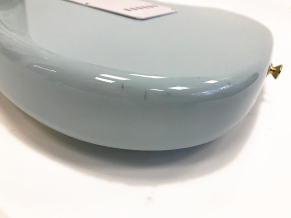 Close-up of light blue electric guitar body corner showing minor scratches and gold strap button on white background