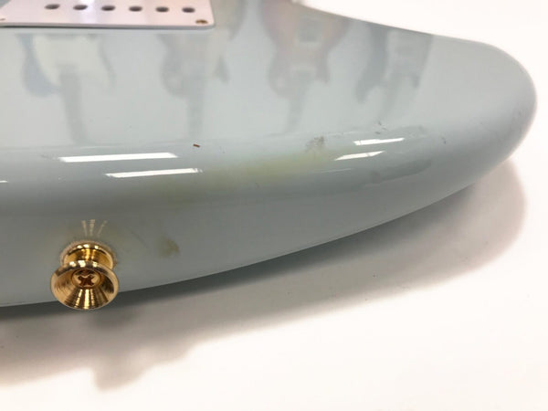 Close-up of light blue guitar body edge with gold strap button and minor surface scratches and discoloration