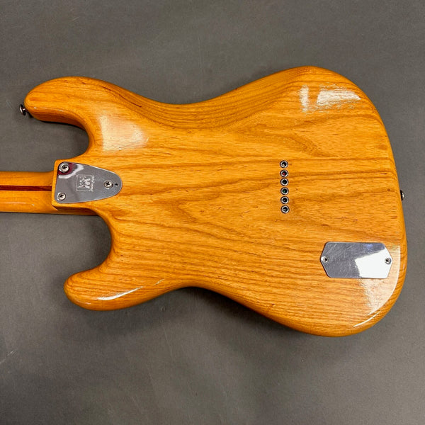 Back view of natural wood electric guitar body showing string ferrules and metal neck plate.
