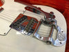 Close-up of white electric guitar bridge with vintage Bigsby-style vibrato tailpiece and single-coil pickups on a red velvet background