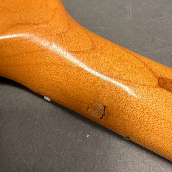 Close-up view of a light brown guitar neck wood grain and finish with natural imperfections and knots against a gray surface background