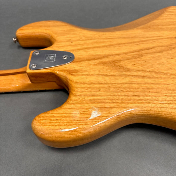 Close-up of the natural wood grain finish on the back of a Coffee House Guitars electric guitar body with chrome neck plate against a gray background