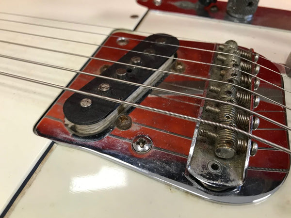 Close-up of vintage guitar bridge and pickup with metal saddle and strings on white electric guitar body showing worn hardware and aged patina
