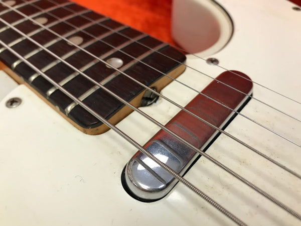 Close-up view of electric guitar fretboard, strings, and vintage single-coil pickup on white body