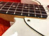 Close-up of electric guitar fretboard with metal strings and white pickguard showing wood grain and frets detail