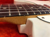 Close-up image of electric guitar neck joint showing rosewood fretboard with metal frets and white body on red background