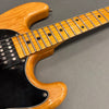 Close-up of natural wood finish electric guitar neck and body with black pickguard and humbucker pickup on gray background