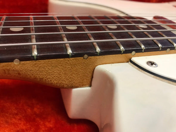 Close-up image of electric guitar neck joint showing rosewood fretboard with metal frets and white body on red background