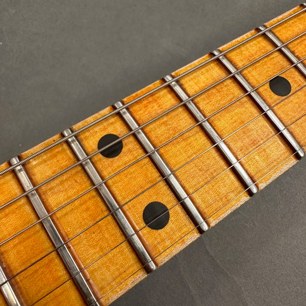 Close-up of guitar fretboard showing maple wood with metal frets, black dot inlays, and steel strings against a dark background, detailed view for electric guitar neck.