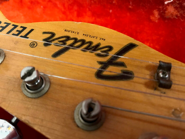 Close-up of a vintage Fender Telecaster guitar headstock with tuning pegs and strings against a red background