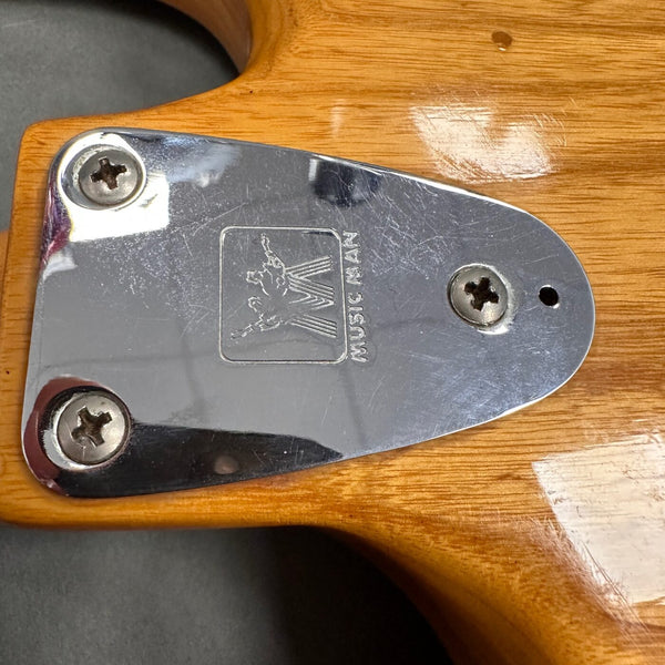 Close-up of Music Man guitar chrome neck plate with logo on natural wood finish guitar body