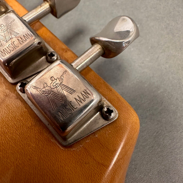 Close-up of vintage Music Man guitar tuning pegs on a natural wood headstock with metal tuning keys and engraved logo