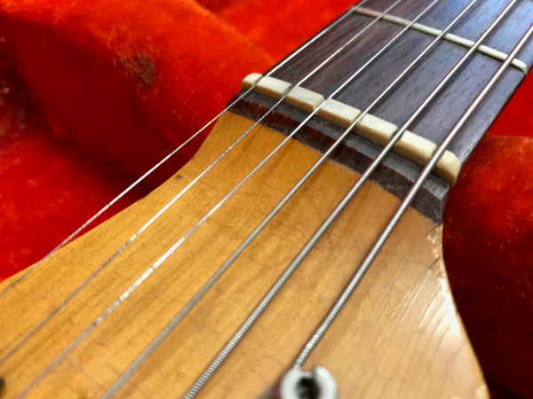 Close-up of vintage guitar nut and strings on wooden fretboard with red velvet background, detailed view of guitar string winding and frets.
