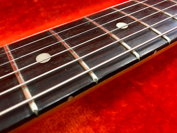 Close-up of acoustic guitar fretboard with metal strings and dot inlays on a red background