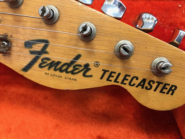 Close-up of vintage Fender Telecaster guitar headstock with tuning pegs and strings on orange background