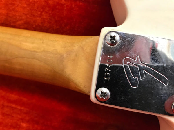 Close-up of electric guitar neck joint with serial number 197404 and metal neck plate with engraved logo on red background