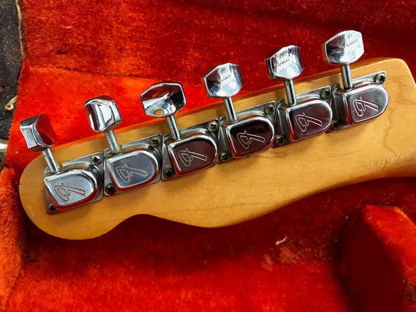 Close-up of six chrome Fender tuning pegs on maple guitar headstock resting on orange plush case lining