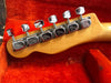 Close-up of vintage Fender guitar tuning pegs on maple headstock with bright red plush guitar case interior background