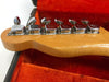 Close-up of vintage Fender guitar headstock tuning pegs with chrome tuning machines and light wood finish resting on an orange plush guitar case interior.