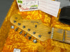 Fender Stratocaster guitar headstock with vintage tuning pegs and maple neck resting in orange plush guitar case with Fender Custom Shop tag and silica gel packet visible