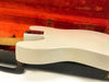 Close-up of vintage white electric guitar body resting in an open red velvet-lined guitar case showing neck joint and metal plate screws