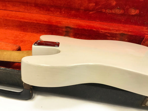 Close-up of vintage white electric guitar body resting in an open red velvet-lined guitar case showing neck joint and metal plate screws