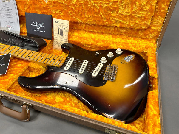 Vintage Fender Stratocaster electric guitar in sunburst finish with maple neck, three single-coil pickups, and white control knobs inside plush orange-lined hardshell case with Fender Custom Care cards and guitar strap