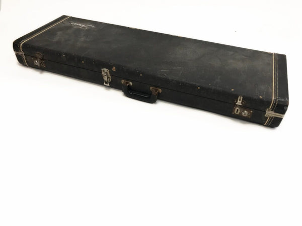 Vintage black rectangular guitar case with metal latches and handle, showing signs of wear and scuffs, isolated on white background
