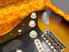 Close-up of vintage electric guitar body showing tone and volume control knobs, pickup, bridge, and sunburst finish with black pickguard inside plush orange-lined guitar case