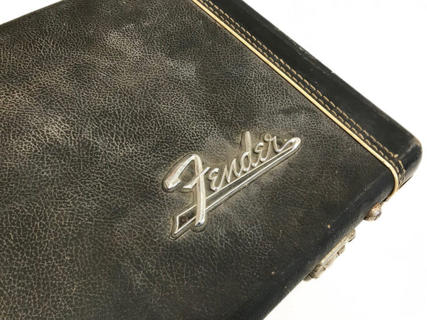 Close-up of vintage black Fender guitar case with silver Fender logo and stitched edges on white background