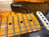Close-up of vintage electric guitar maple fretboard with metal frets and worn strings, black body, and white single-coil pickup on yellow plush case background