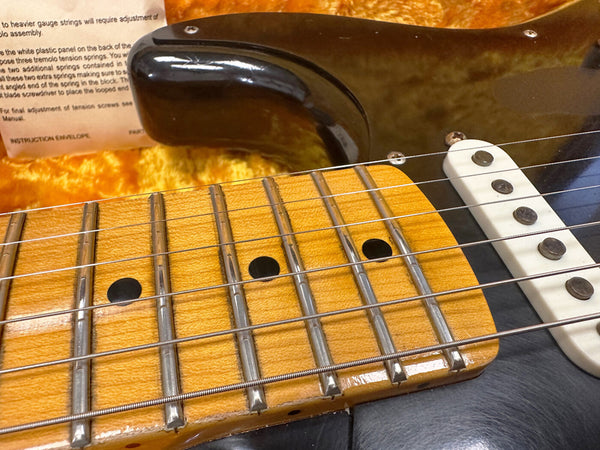 Close-up of vintage electric guitar maple fretboard with metal frets and worn strings, black body, and white single-coil pickup on yellow plush case background