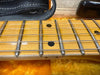 Close-up of maple guitar fretboard with silver frets and black dot inlays, six steel strings, and black leather strap on bright orange plush case lining