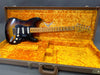 Vintage Fender Stratocaster electric guitar in sunburst finish with maple neck and black pickguard resting in open plush orange Fender guitar case