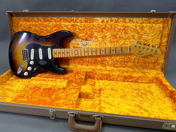 Vintage Fender Stratocaster electric guitar in sunburst finish with maple neck and black pickguard resting in open plush orange Fender guitar case