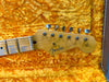 Close-up of Fender Stratocaster guitar headstock with tuning pegs and "Original Contour Body" text on yellow plush guitar case interior
