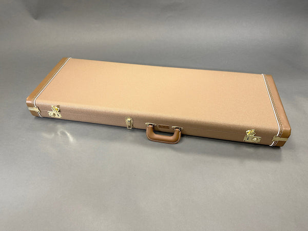Closed rectangular brown hard guitar case with leather handle and gold latches on gray background