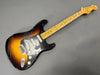 Fender Stratocaster electric guitar with sunburst finish, maple neck, three single-coil pickups, black pickguard, and vintage wear and aging on the body and headstock.