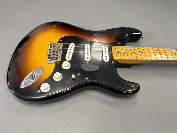 Vintage sunburst electric guitar with black pickguard and three single-coil pickups, maple neck with dot inlays, showing wear and paint chips on the body.